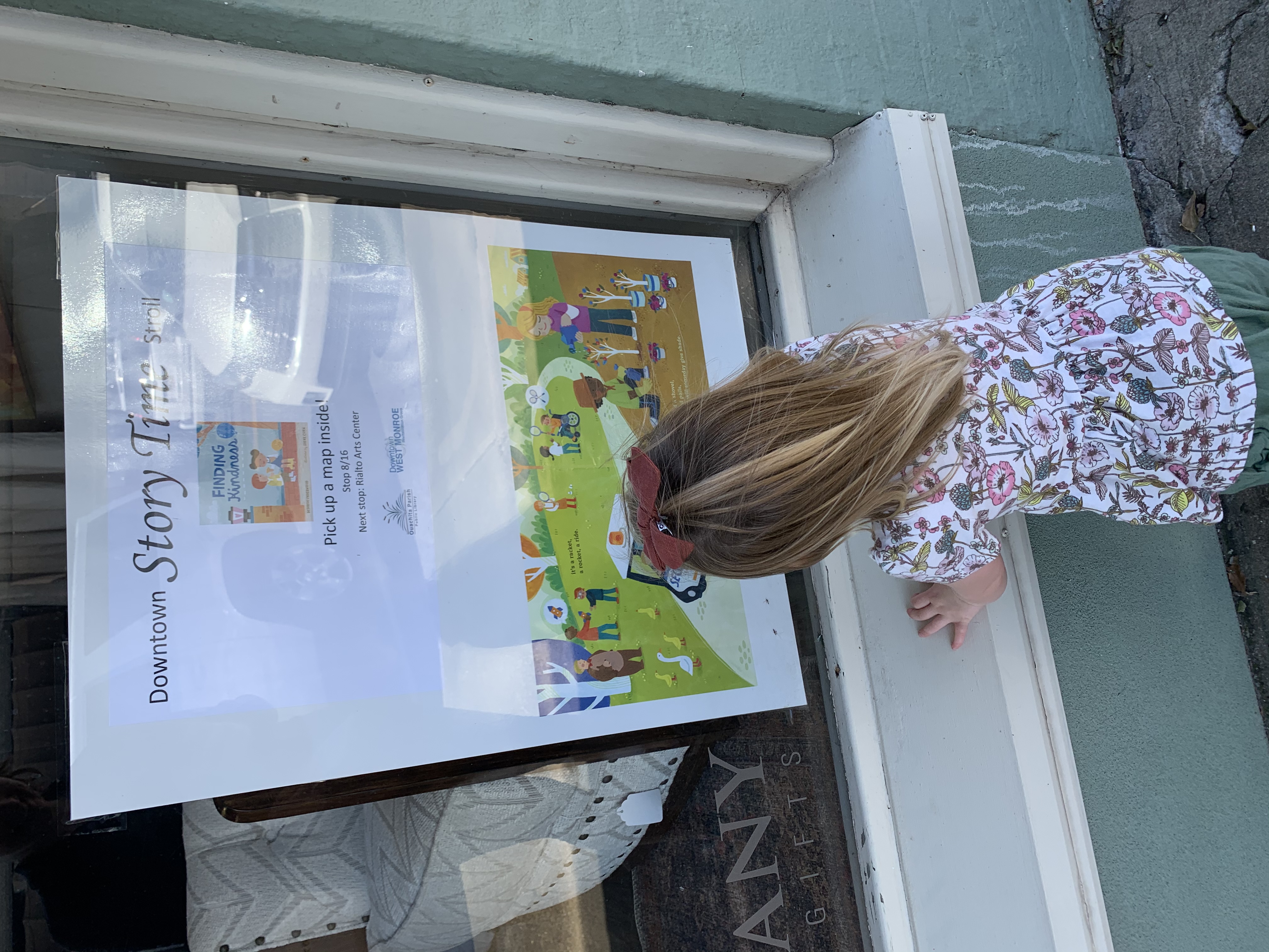 A young child stands in front of a store window. A book page is posted in the window.