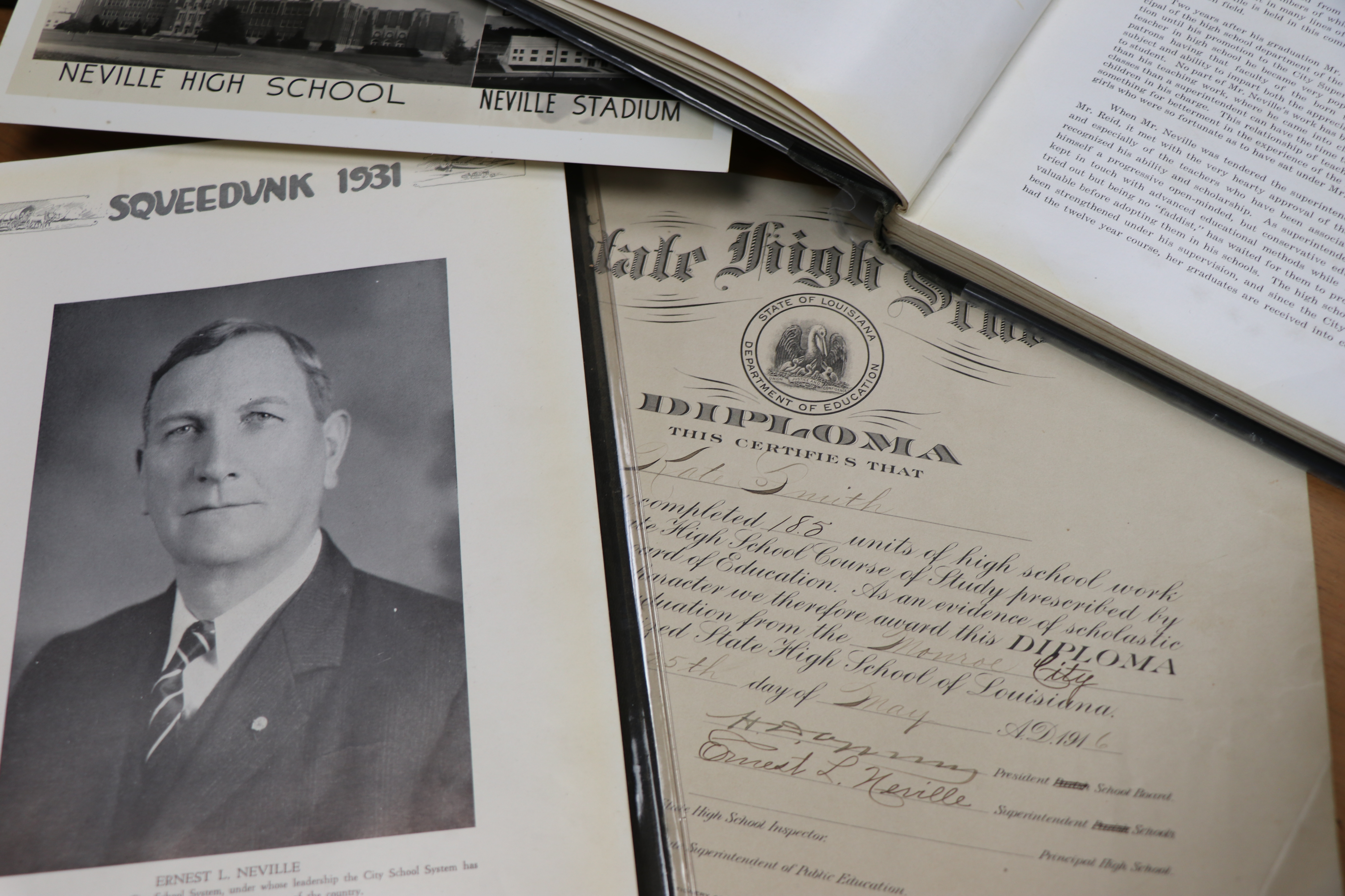 A table featuring various historical items:a 1931 Squeedunk yearbook open to a portrait of Ernest Long Neville, a high school diploma, and more