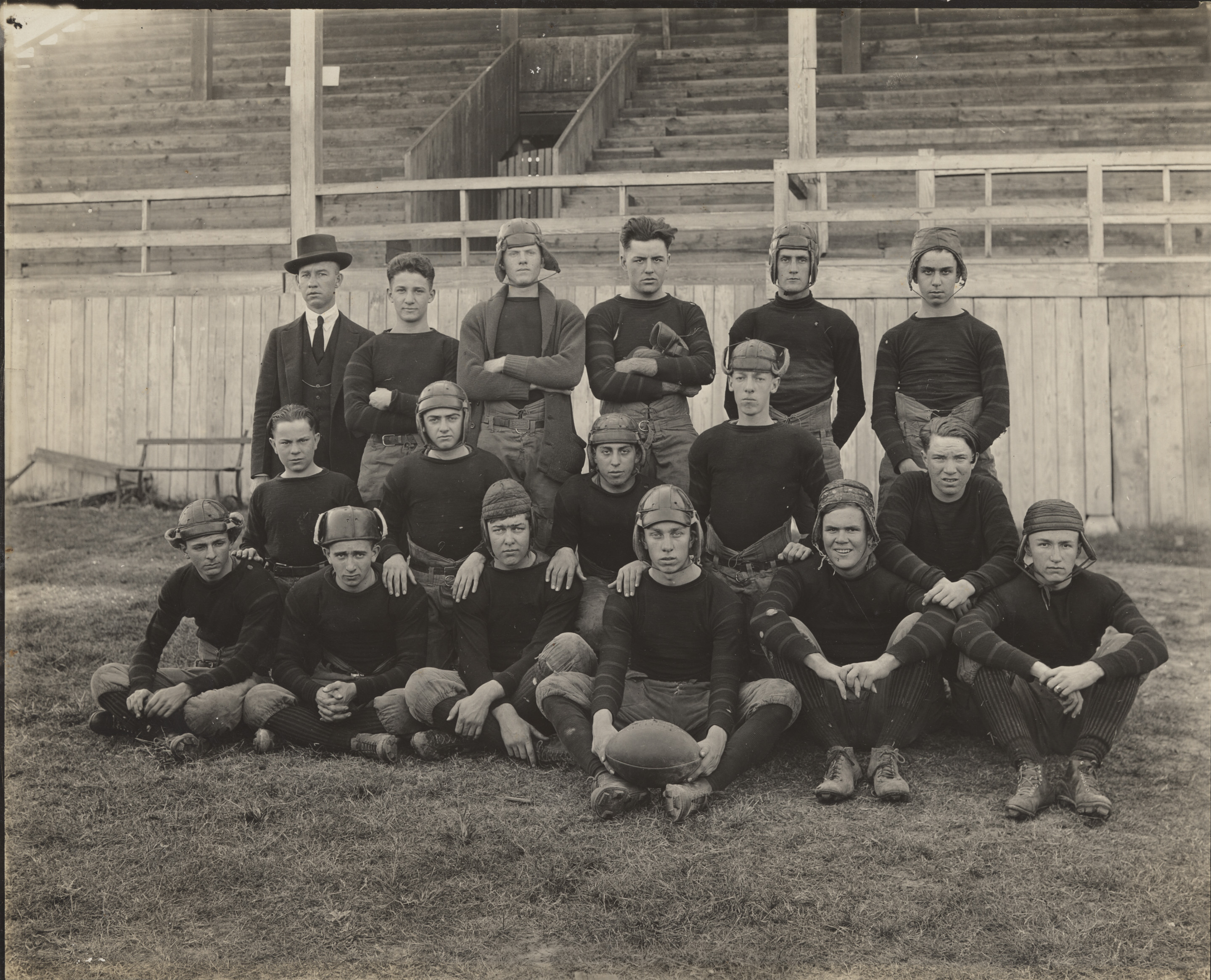 A black and white image of teenage boys in old school football uniforms. The boys pose on a field.