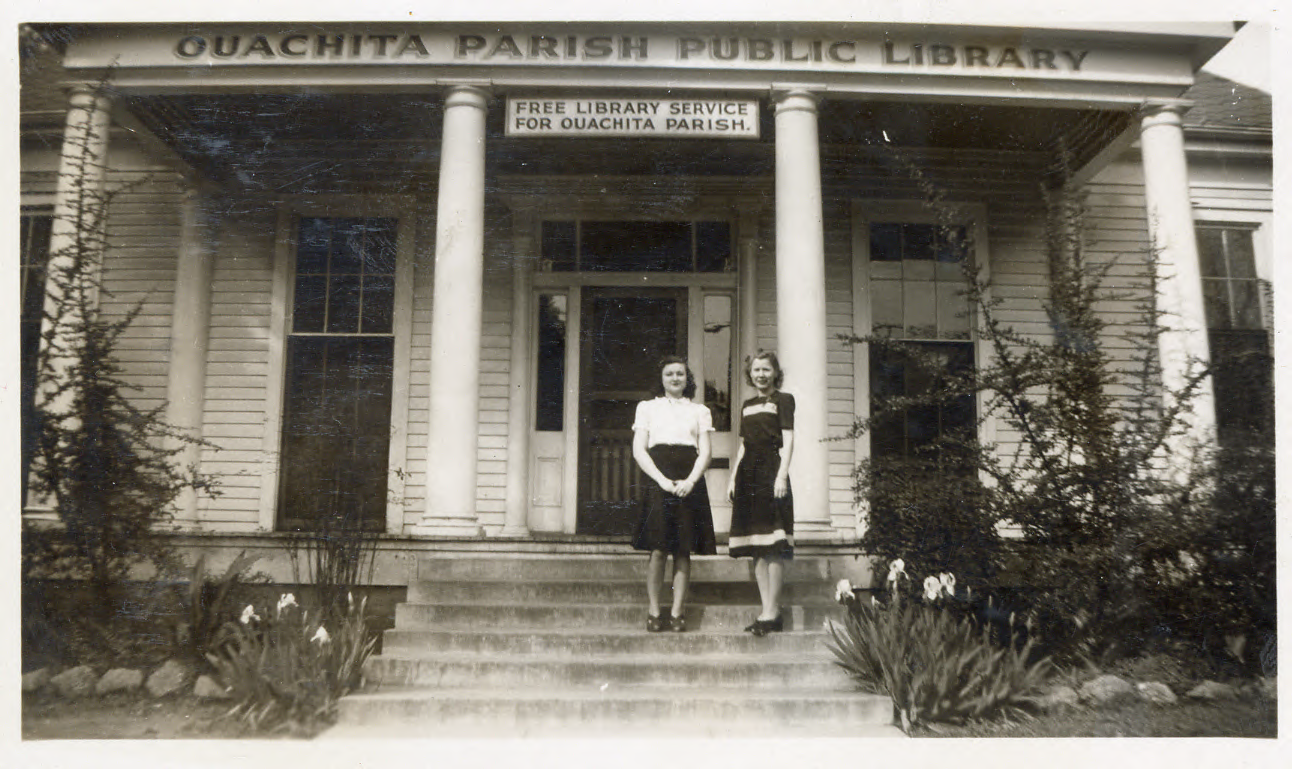 Two women stand in front of a library