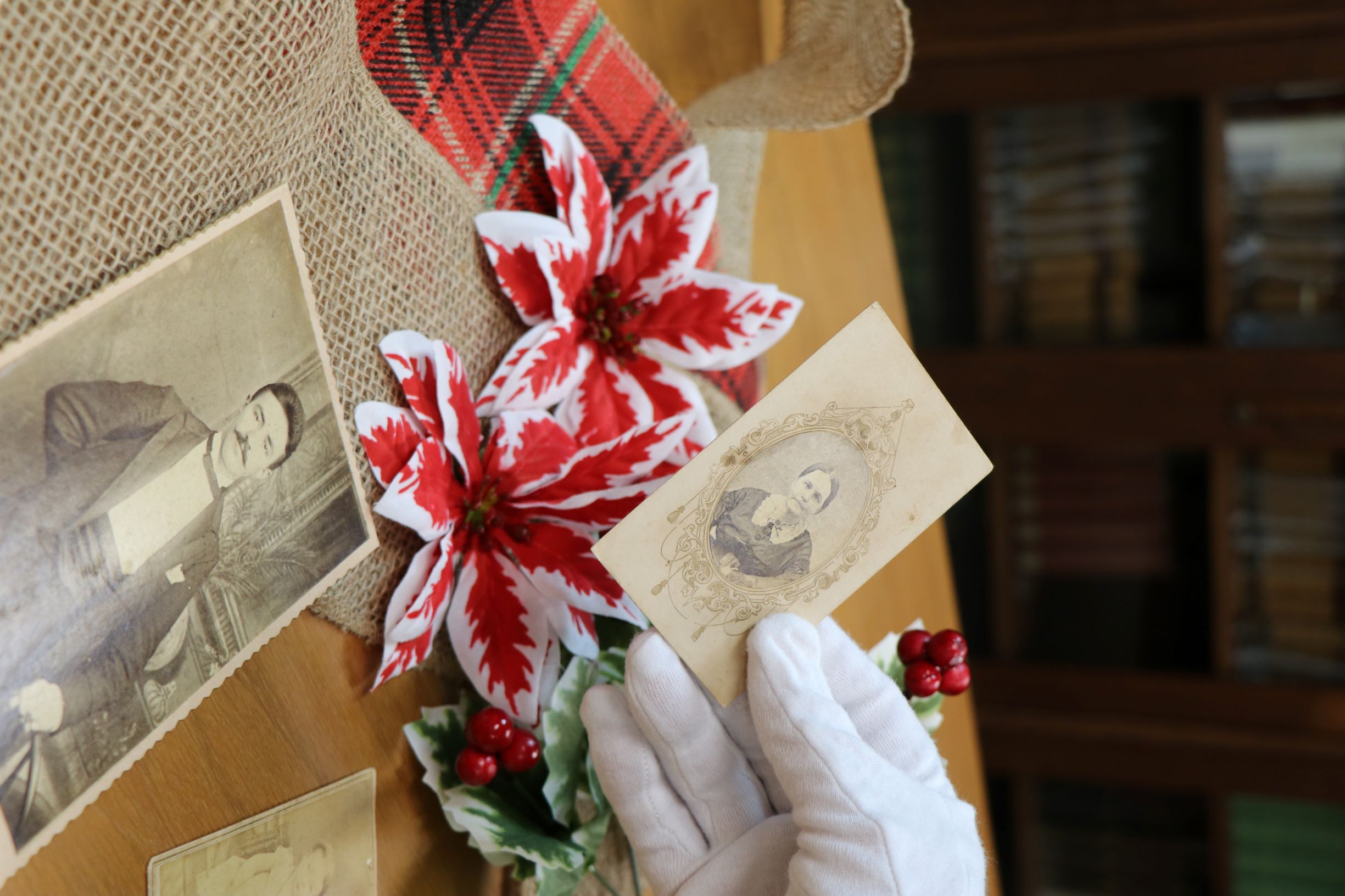 A gloved hand holds an old black and white photo. More old pictures lay on a table decorated with burlap and flowers.